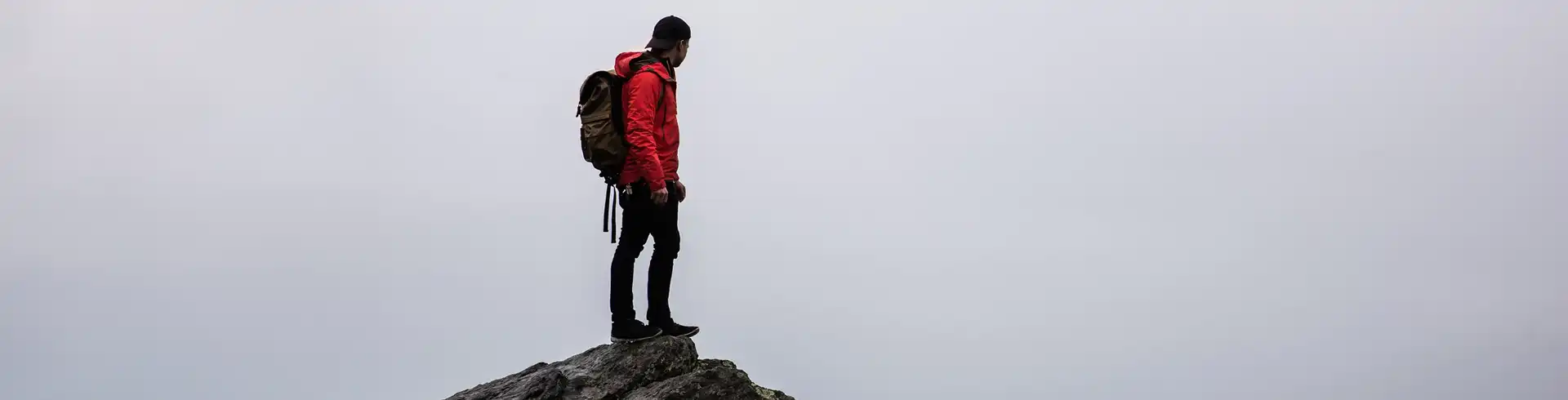 Foto av en person med tursekk som står på et fjell og ser på utsikten